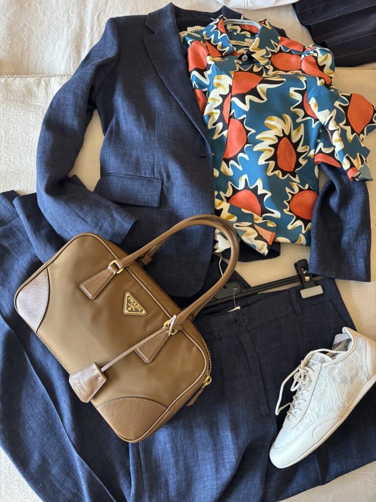 Blauer Anzug kombiniert mit gemusterter Bluse, Sneakern und beiger Tasche – modernes Anlass-Outfit mit Basics